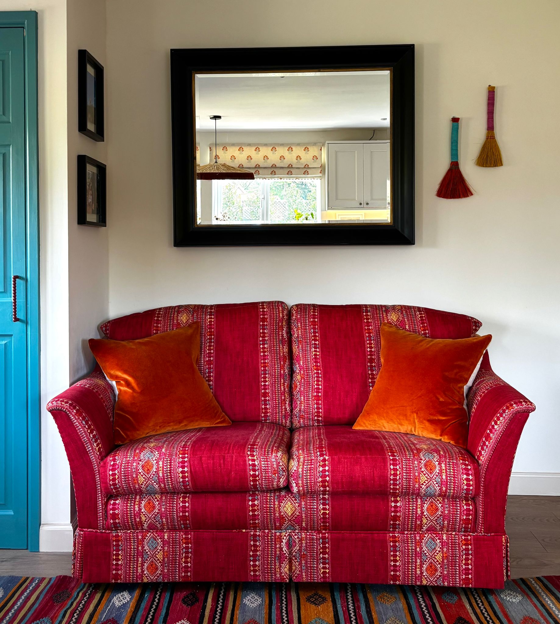 Deep red patterned sofa layered with orange velvet cushions, set against a teal blue door and framed mirror